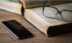 eyeglasses on top of a bool with a cellphone beside