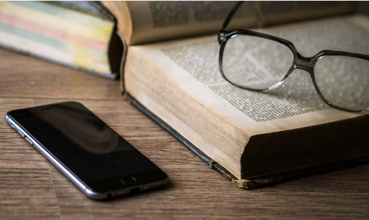 eyeglasses on top of a bool with a cellphone beside