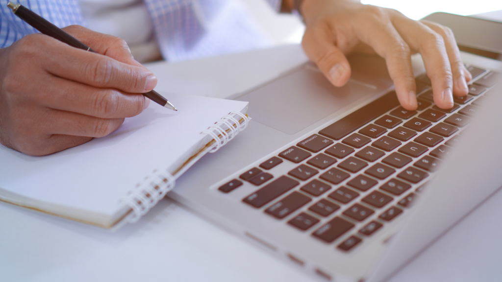 left hand on laptop while right hand is holding a pen