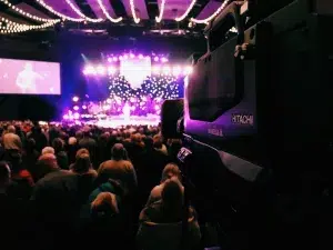 video camera with people looking at the stage