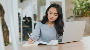 Woman Writing on Her Notebook and Using Her Laptop Outdoors