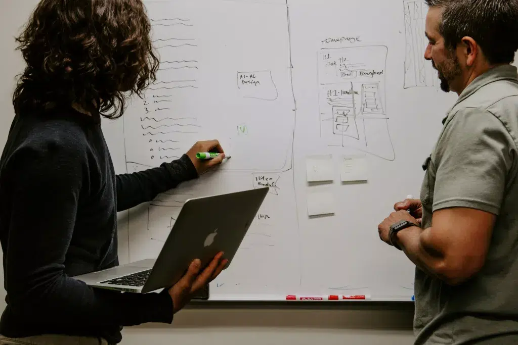 woman writing on the board while holding a laptop