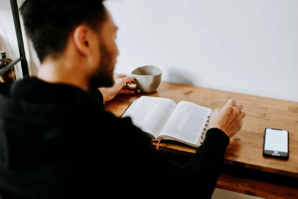 man reading the bible with phone beside