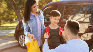 woman holding a yellow bag while the man is fixing the red backpack of the child