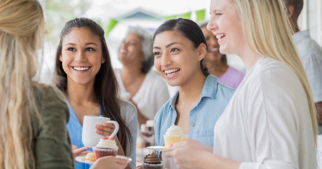 Four women smiling and talking at an event with cupcakes.