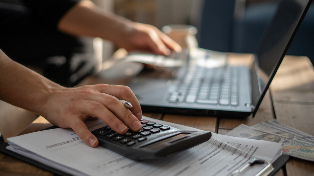 man on laptop while holding a pen with calculator