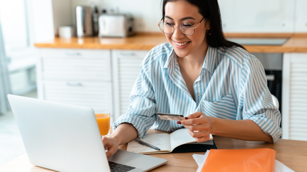 Woman Using Laptop while Holding Credit Card in Kitchen